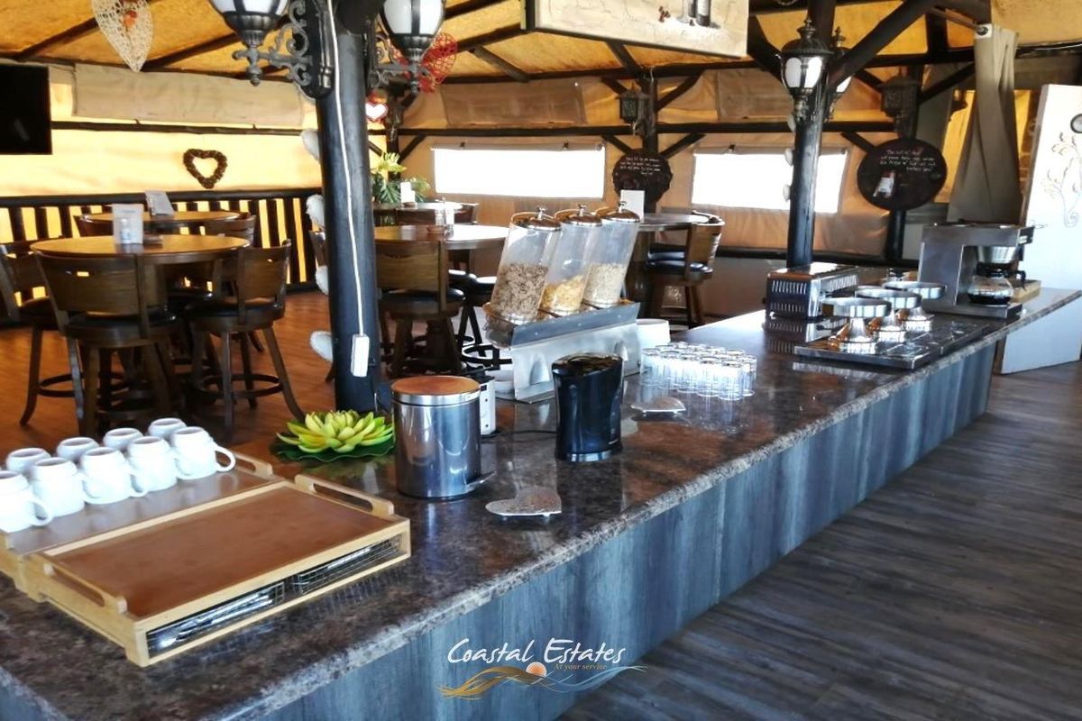 A rustic-style breakfast serving area featuring a long granite countertop, timber support beams, and an open-plan layout suitable for guest house dining.