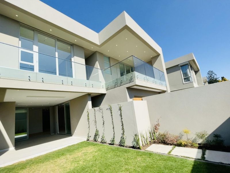 Modern double-story cluster home featuring a spacious covered patio, glass-railed balcony, and a well-maintained private garden.