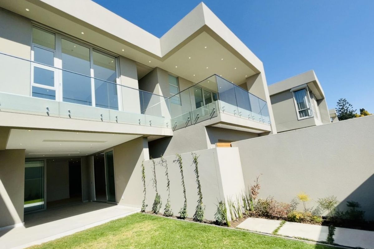 Modern double-story cluster home featuring a spacious covered patio, glass-railed balcony, and a well-maintained private garden.