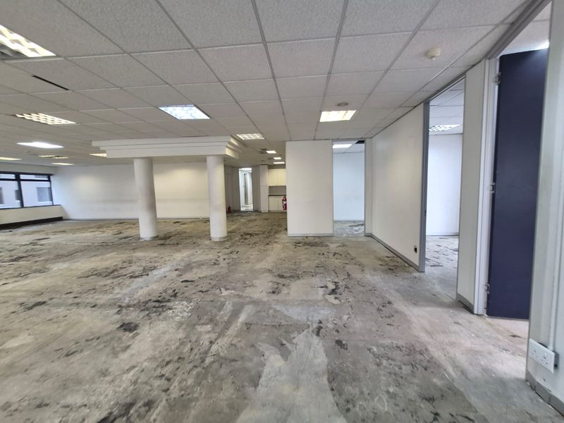 An expansive, vacant office space featuring a suspended ceiling, recessed lighting, and structural columns, requiring new flooring and cosmetic updates.