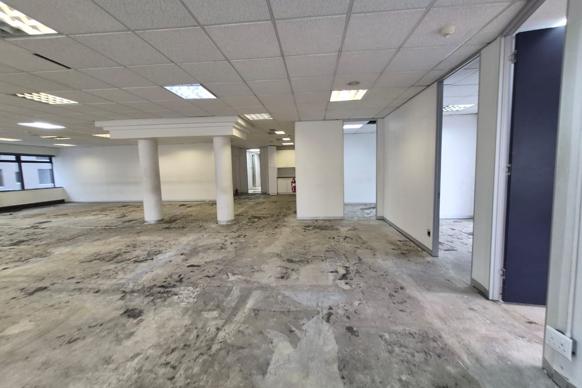An expansive, vacant office space featuring a suspended ceiling, recessed lighting, and structural columns, requiring new flooring and cosmetic updates.