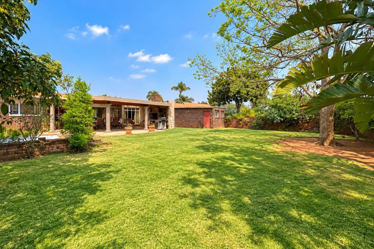 Spacious rear garden featuring a well-maintained lawn, mature trees, and a covered patio area with a built-in braai, perfect for outdoor entertaining.