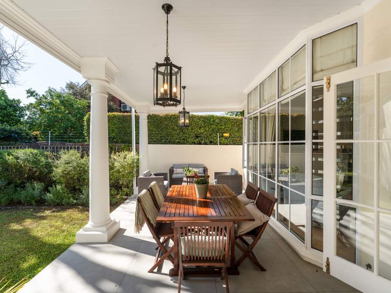 A spacious covered patio featuring classic columns, elegant pendant lighting, and large glass french doors leading into the home, overlooking a private garden.