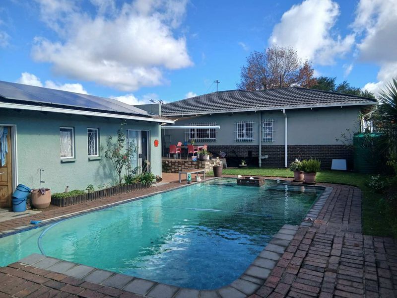 Rear exterior view featuring a swimming pool, brick paved surround, and a covered patio area attached to the main house structure.