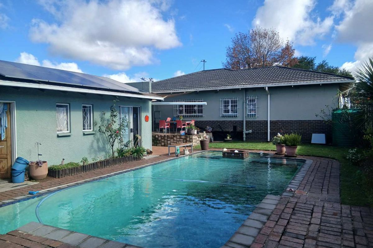 Rear exterior view featuring a swimming pool, brick paved surround, and a covered patio area attached to the main house structure.