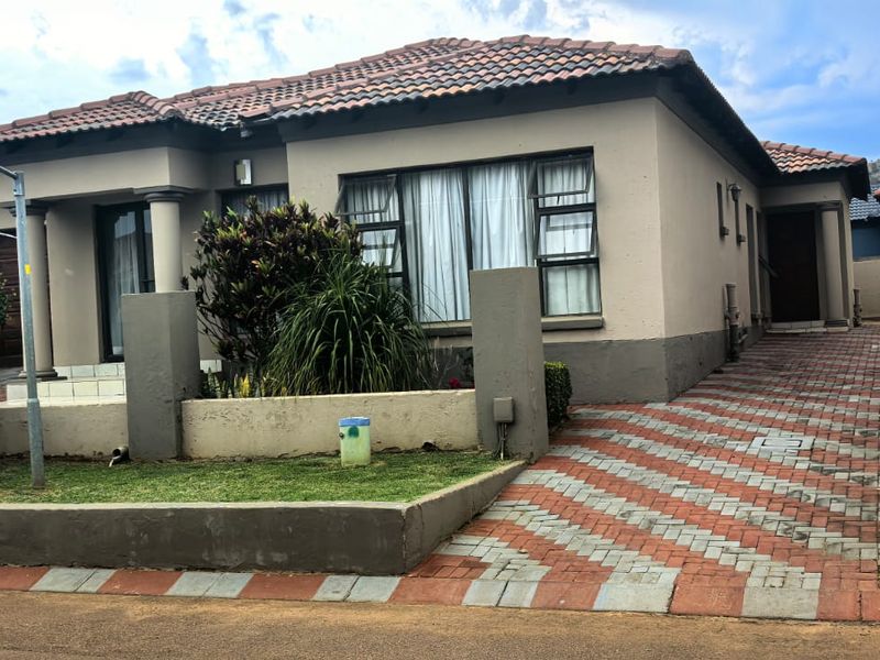 Front elevation of a single-story house featuring a tiled roof, paved driveway, and a low boundary wall with integrated pillars.
