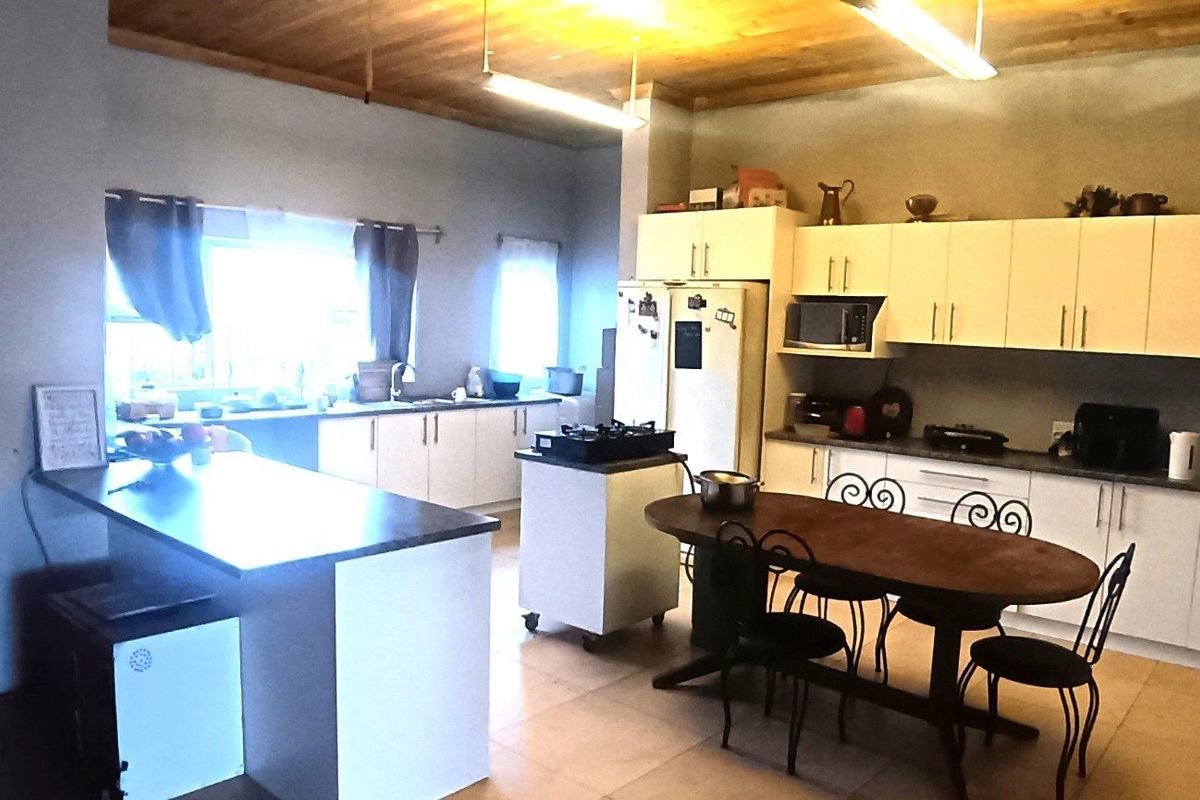 Spacious kitchen featuring white cabinetry, a central island, timber ceiling, and tiled flooring, offering a functional layout with ample storage and workspace.