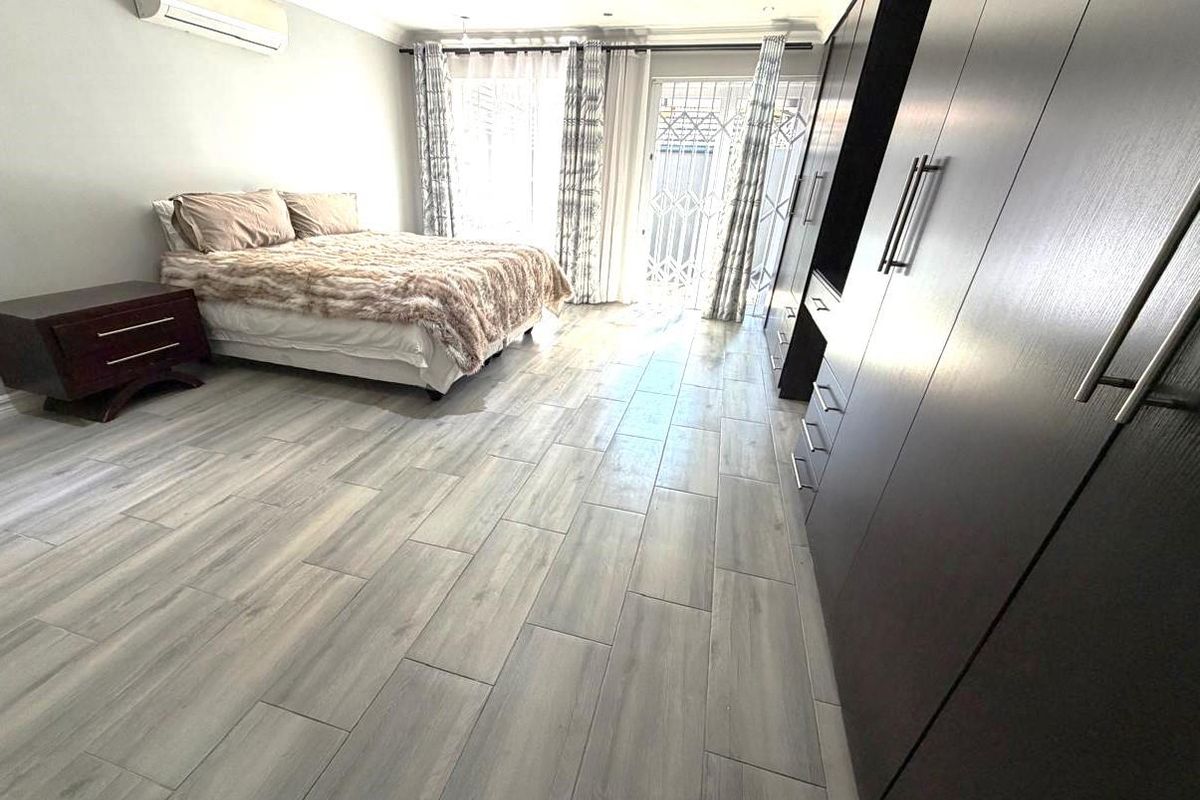 Spacious bedroom featuring modern wood-look tiled flooring, extensive built-in cupboards, an air conditioning unit, and direct access to the exterior via a sliding door.