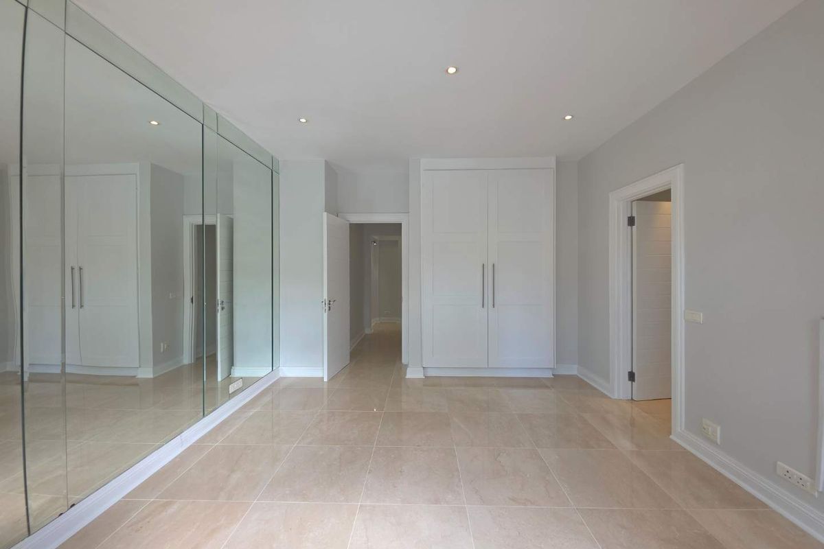 A bright, modern bedroom featuring large floor-to-ceiling mirrored wardrobe doors, neutral tiled flooring, and built-in cabinetry, offering a clean and spacious aesthetic.