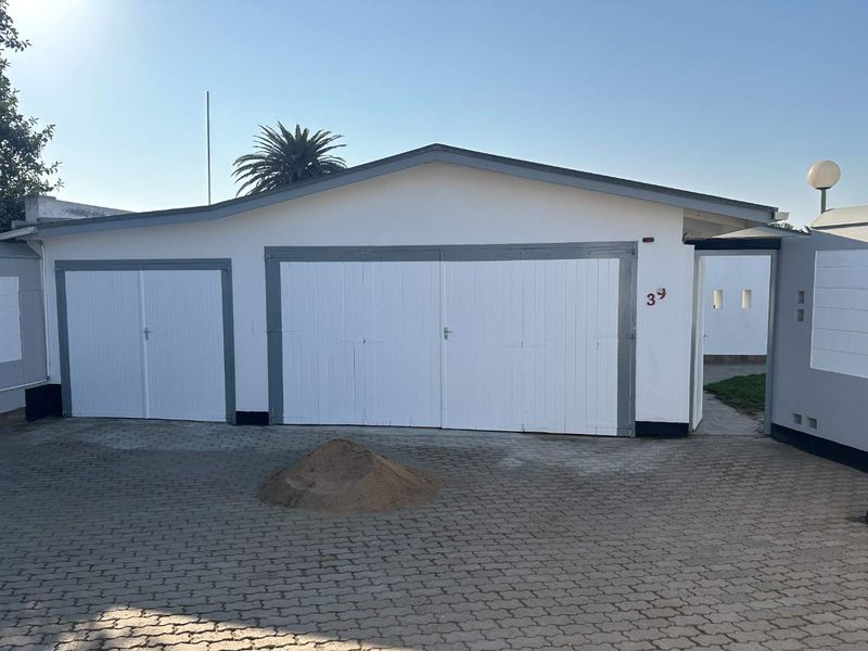 A detached garage structure featuring a double and single garage door, set on a paved driveway with a surrounding boundary wall.