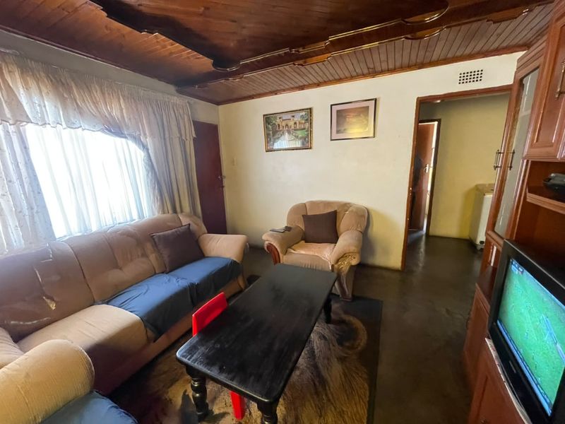 A living room featuring a timber tongue and groove ceiling and concrete flooring, offering a dated aesthetic ready for modernization.