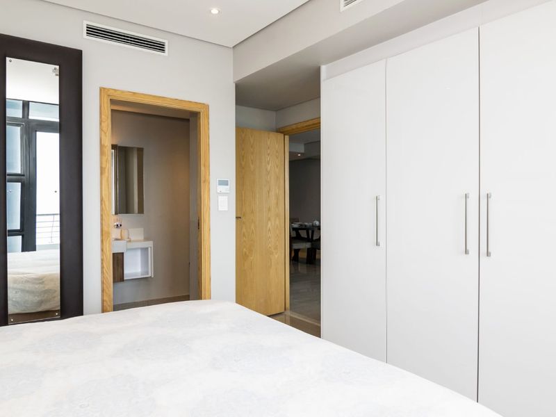 Modern bedroom featuring extensive built-in white cabinetry, recessed lighting, ducted air conditioning, and direct access to an en-suite bathroom.