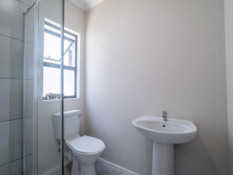 A clean and functional bathroom featuring a pedestal basin, toilet, and a glass-enclosed shower with neutral wall tiling.