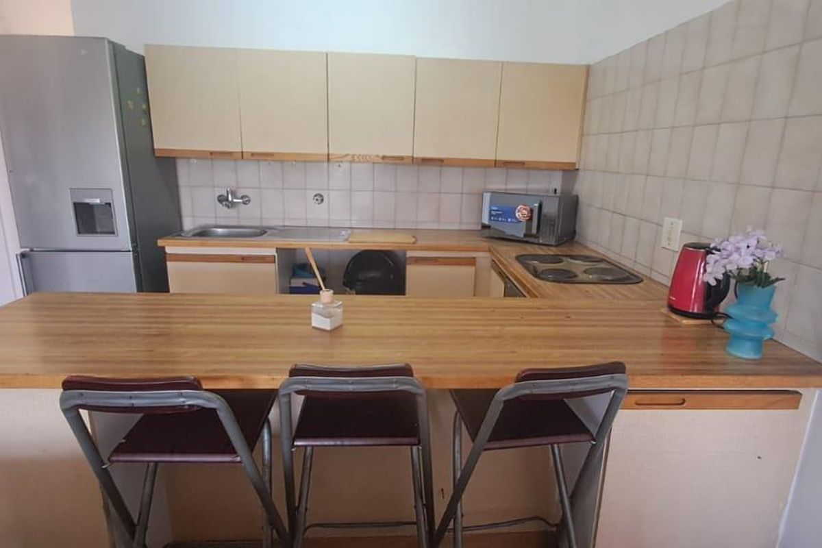 A functional kitchen featuring laminate countertops, built-in cabinetry, a tiled backsplash, and an integrated electric hob with a breakfast bar area.