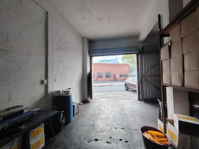 Industrial garage or warehouse space featuring concrete flooring, exposed walls, and a large roller shutter door providing direct street access.