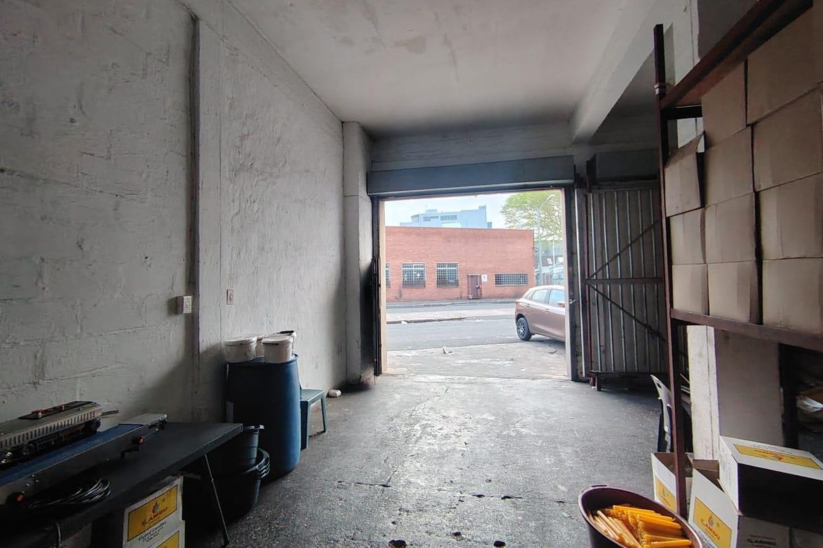 Industrial garage or warehouse space featuring concrete flooring, exposed walls, and a large roller shutter door providing direct street access.