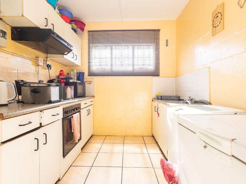 A compact kitchen featuring built-in cabinetry, an integrated oven with extractor fan, tiled flooring, and a functional sink area.