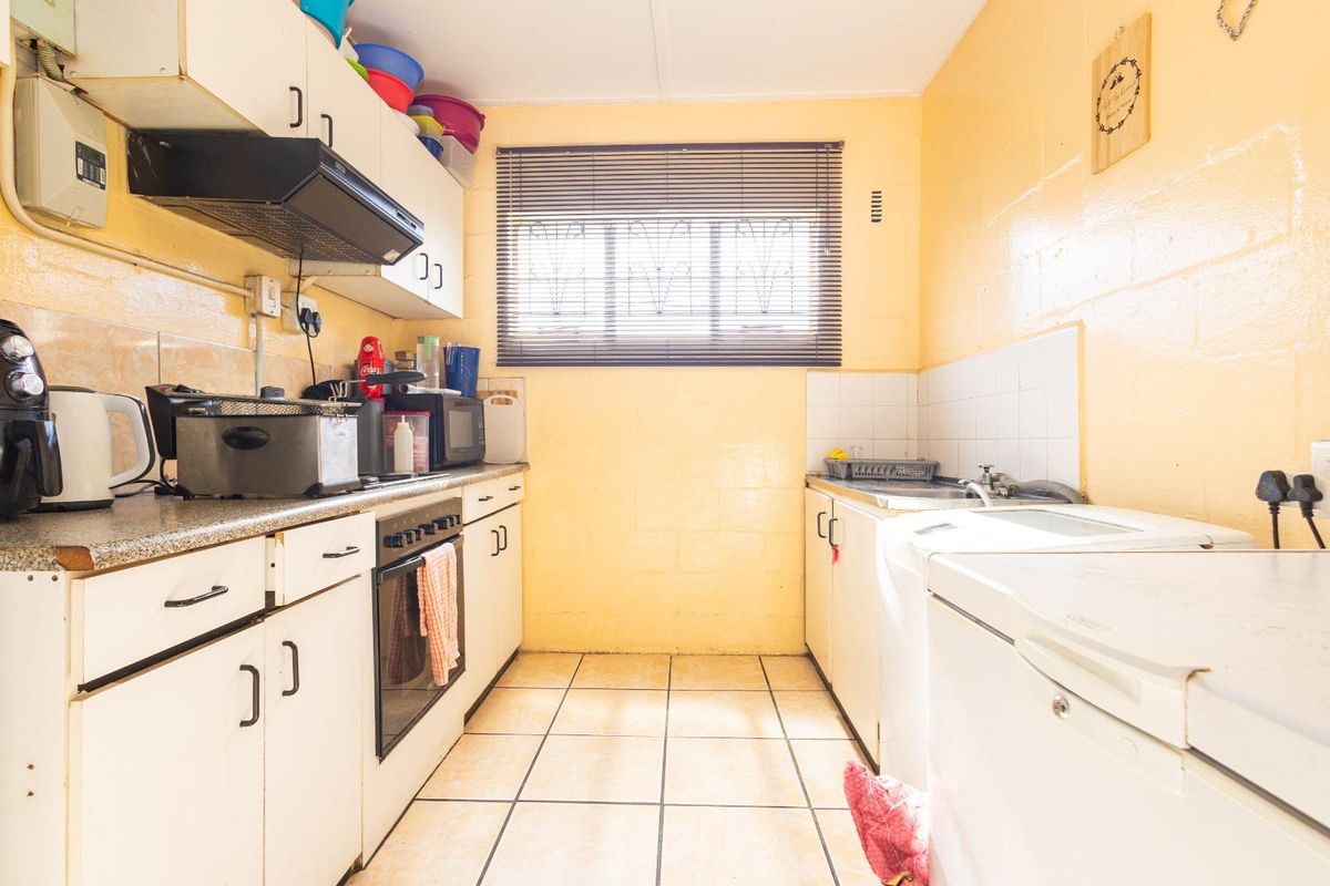 A compact kitchen featuring built-in cabinetry, an integrated oven with extractor fan, tiled flooring, and a functional sink area.
