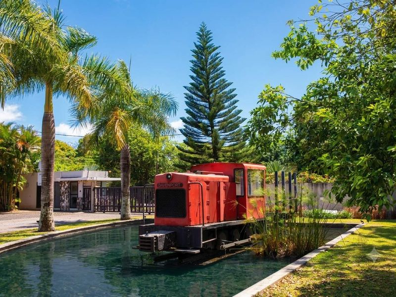A well-maintained garden featuring a decorative water feature with a vintage locomotive display, mature palm trees, and secure perimeter walling.