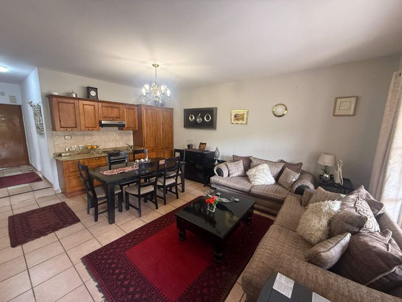 Open-plan living and dining area featuring a compact kitchen with wooden cabinetry, granite countertops, and tiled flooring throughout.