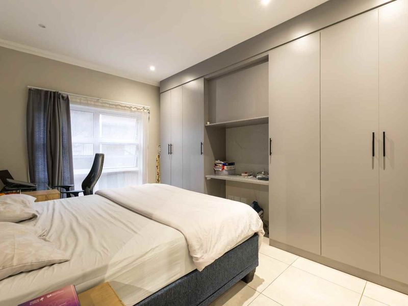 A well-maintained bedroom featuring modern grey built-in cupboards, a convenient integrated desk space, tiled flooring, and recessed lighting.