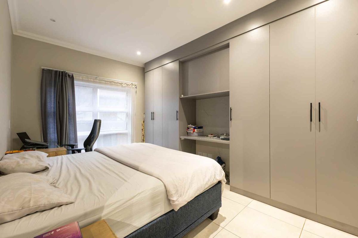 A well-maintained bedroom featuring modern grey built-in cupboards, a convenient integrated desk space, tiled flooring, and recessed lighting.