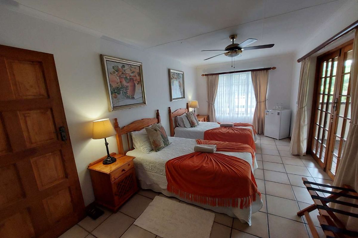 A spacious bedroom featuring tiled flooring, a ceiling fan, and direct access to an outdoor area through wooden french doors.