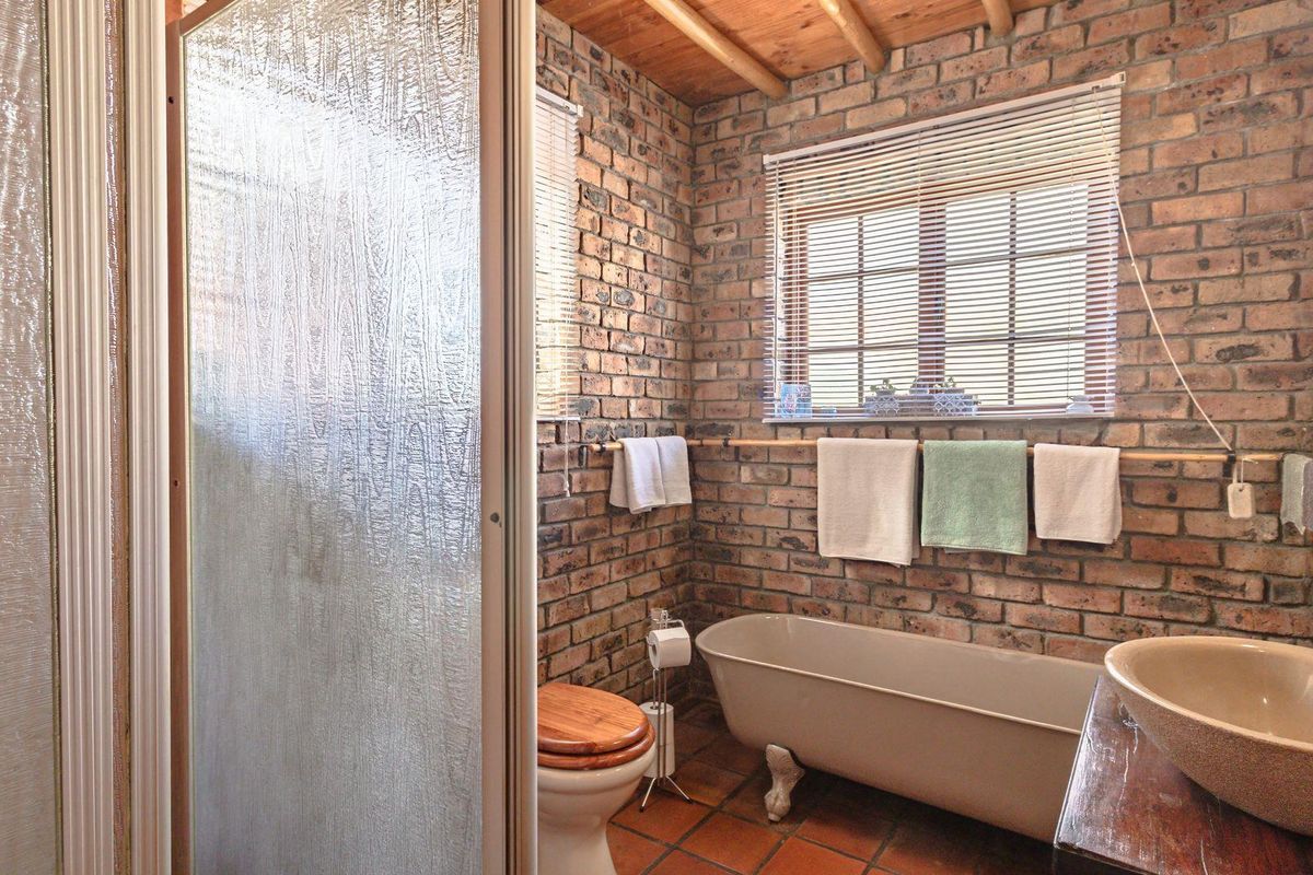 A rustic-style bathroom featuring exposed brick walls, a clawfoot bathtub, a vessel sink, and a separate shower enclosure with a textured glass door.
