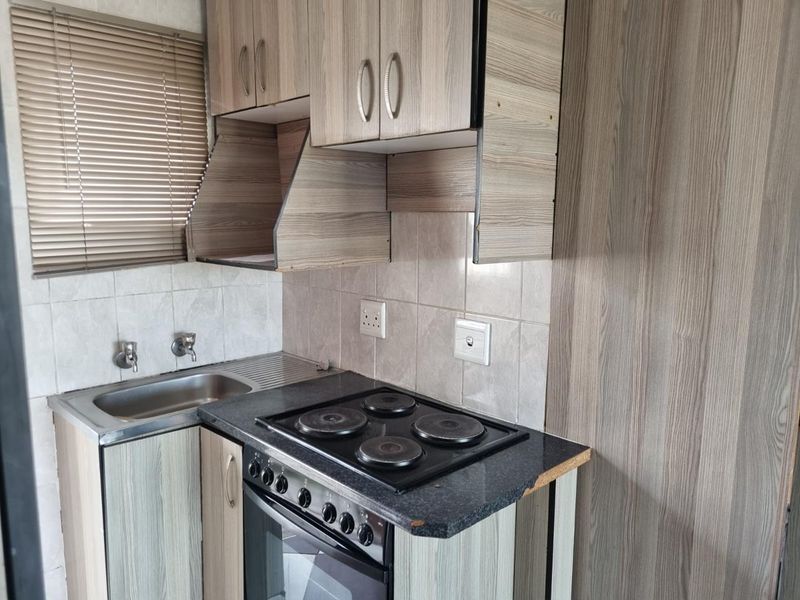 Compact kitchen featuring wood-look cabinetry, a built-in electric oven and hob, stainless steel sink, and tiled backsplash.