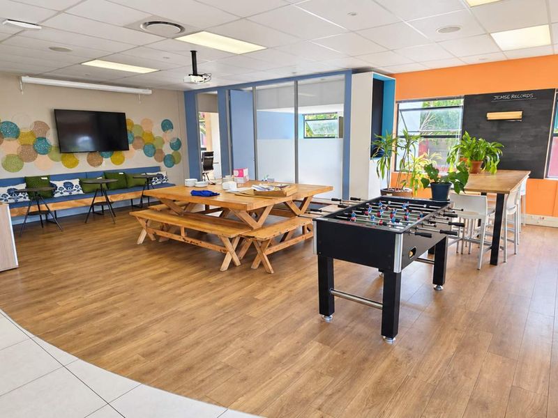 A bright, open-plan office breakout area featuring laminate flooring, a suspended ceiling, built-in bench seating, and a dedicated chalkboard wall.