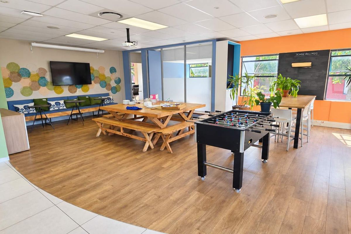 A bright, open-plan office breakout area featuring laminate flooring, a suspended ceiling, built-in bench seating, and a dedicated chalkboard wall.