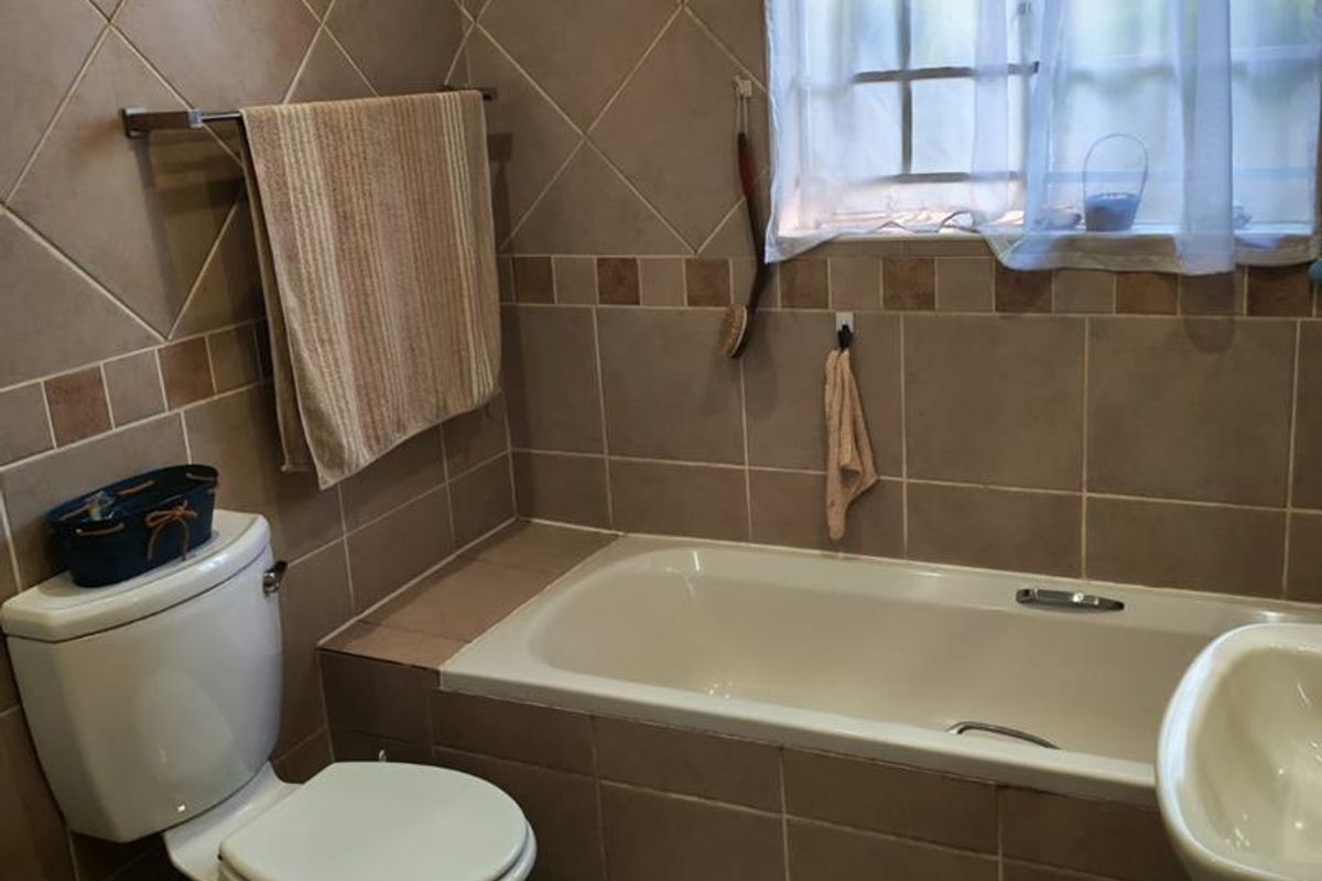 A functional bathroom featuring a built-in bathtub, pedestal basin, and toilet with neutral ceramic wall and floor tiling.