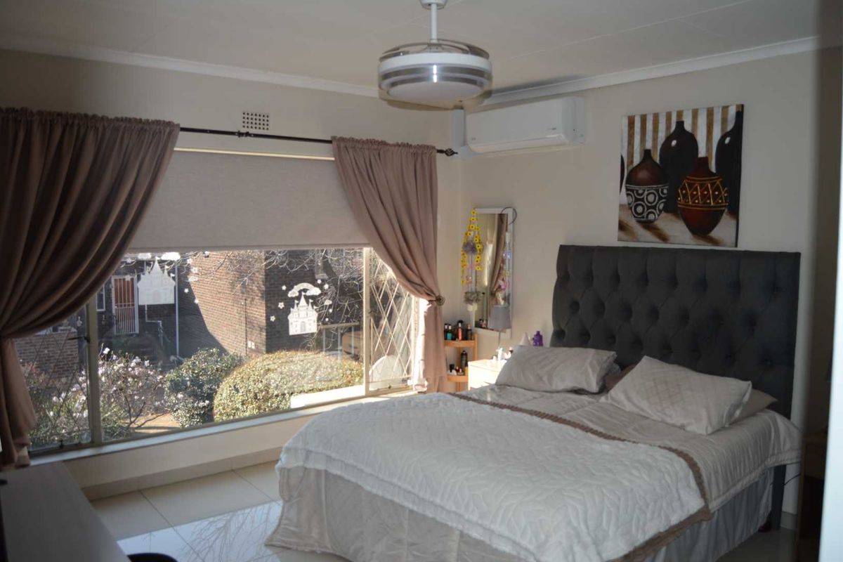 A well-lit bedroom featuring a large window, tiled flooring, and a wall-mounted air conditioning unit.