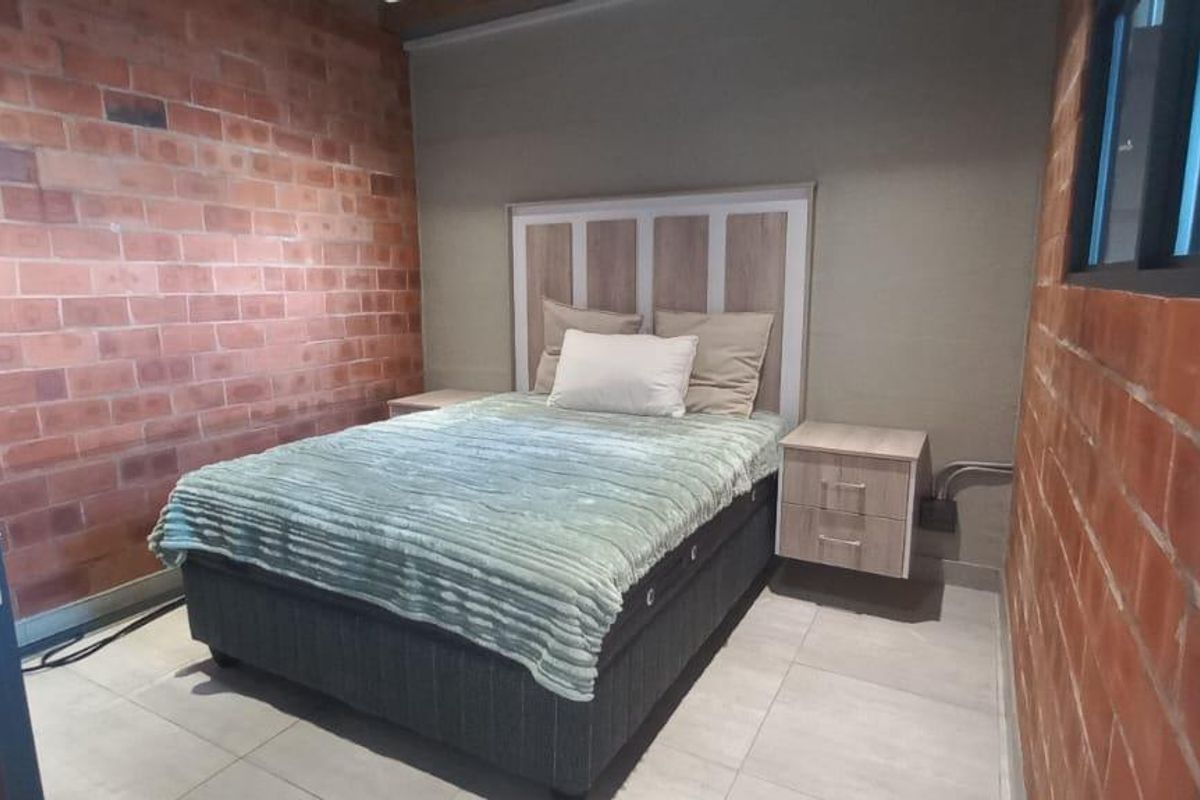 A bedroom featuring exposed brick walls, tiled flooring, and a modern headboard with integrated bedside storage.