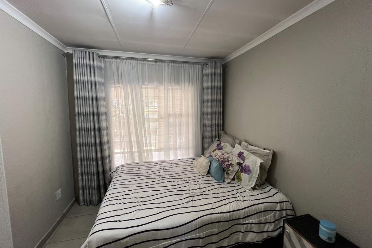 A functional bedroom featuring tiled flooring, neutral wall finishes, and large windows with installed curtain rails, providing a comfortable and well-lit living space.