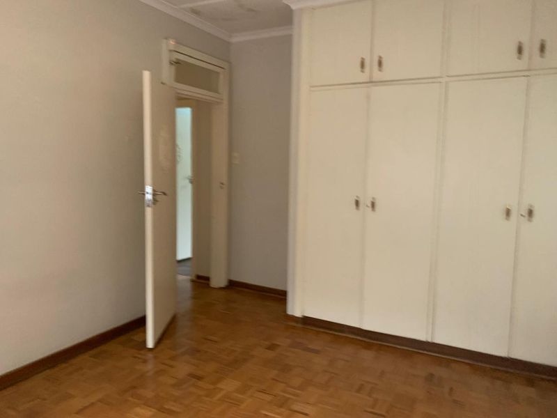 An empty bedroom featuring parquet flooring and built-in cupboards, showing signs of ceiling water damage.