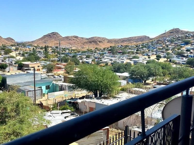 Elevated view overlooking the surrounding residential neighbourhood and distant hills, captured from a balcony with a metal railing.