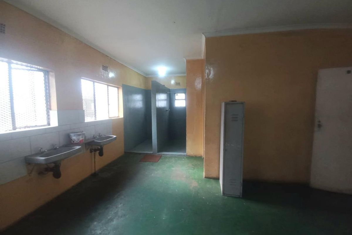 Industrial-style communal bathroom facility featuring wall-mounted sinks, partitioned shower cubicles, and durable painted concrete flooring.