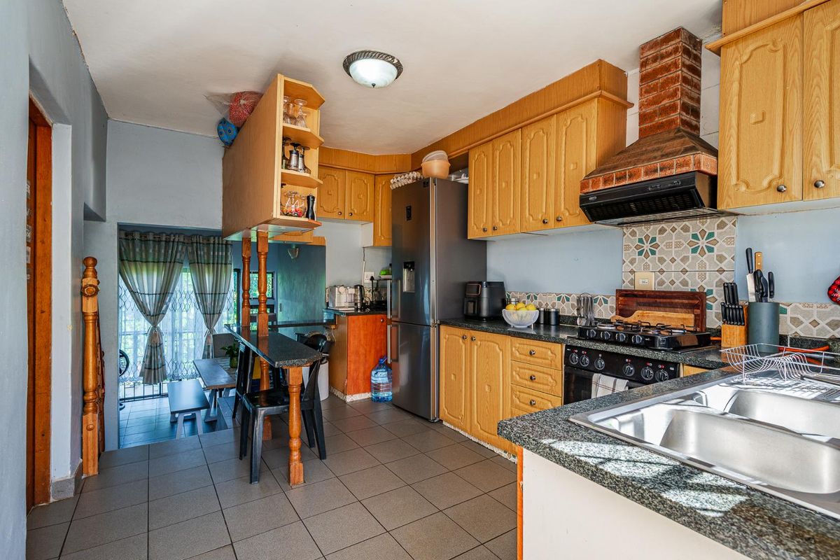 A functional kitchen featuring wooden cabinetry, granite countertops, a built-in gas hob with brick-style extractor hood, and tiled flooring.