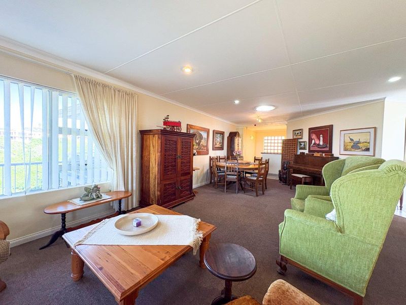 Spacious open-plan living and dining area featuring neutral walls, carpeted flooring, and large windows providing ample natural light.