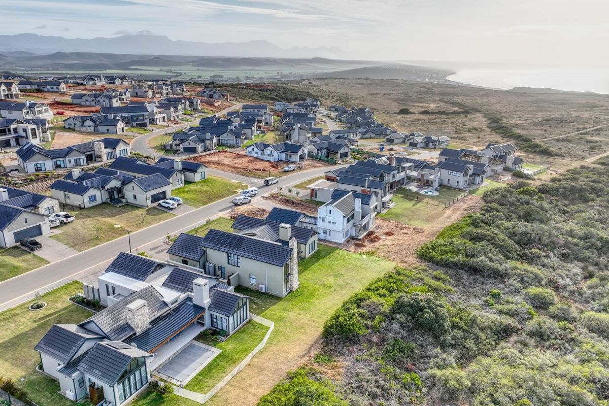 Aerial view of a modern residential estate featuring contemporary homes, paved roads, and surrounding natural coastal landscape.