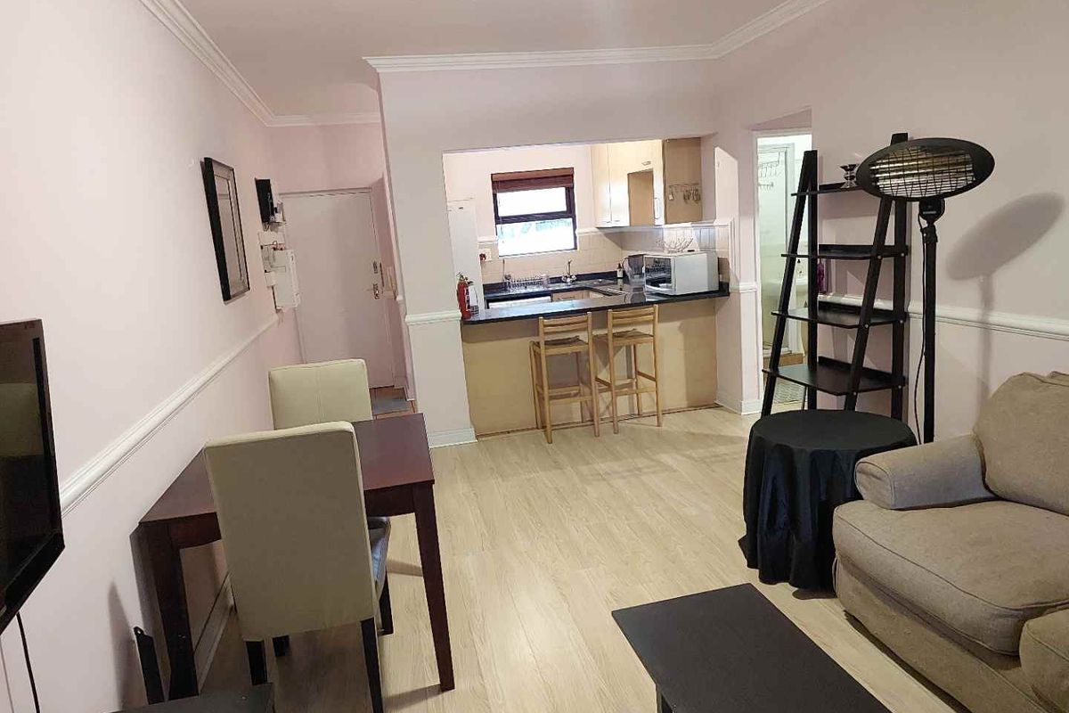 Open-plan living and dining area flowing into a functional kitchen with a breakfast counter and light-toned laminate flooring.