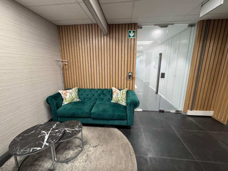 Modern office reception area featuring timber slat wall paneling, sleek glass partition doors, and dark tiled flooring.