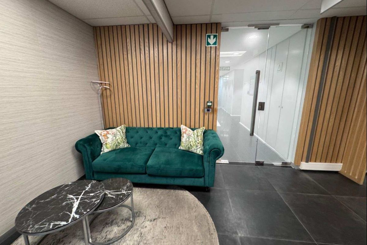 Modern office reception area featuring timber slat wall paneling, sleek glass partition doors, and dark tiled flooring.