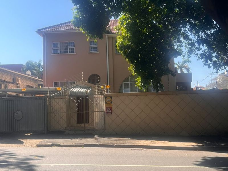 Front elevation of a multi-story house featuring a perimeter wall with electric fencing and a secure gated entrance.