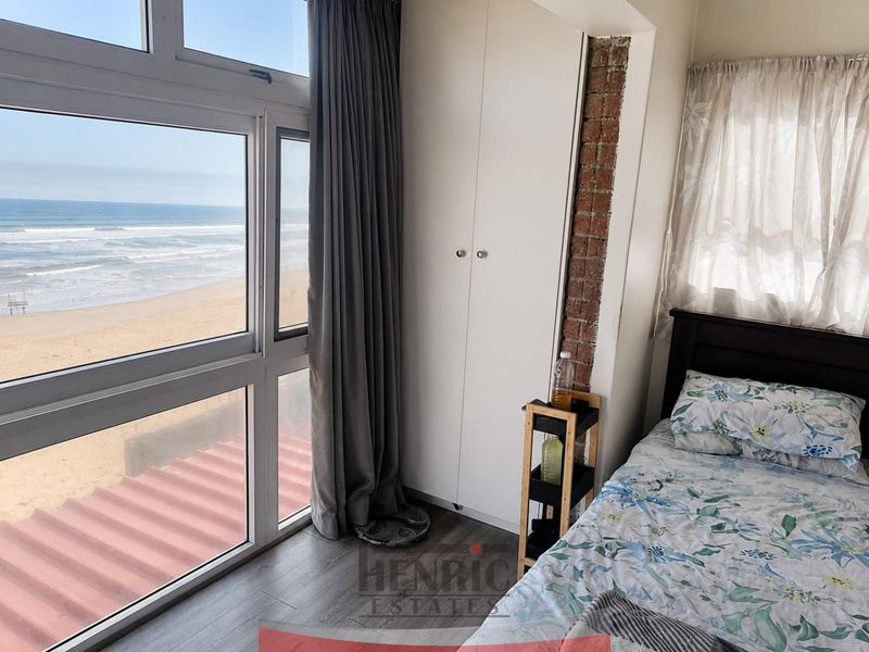 Bedroom featuring large floor-to-ceiling windows with direct ocean views, built-in wardrobe, and an exposed brick feature wall.