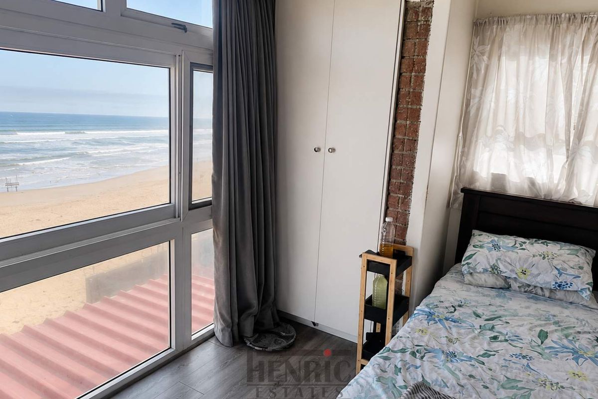 Bedroom featuring large floor-to-ceiling windows with direct ocean views, built-in wardrobe, and an exposed brick feature wall.