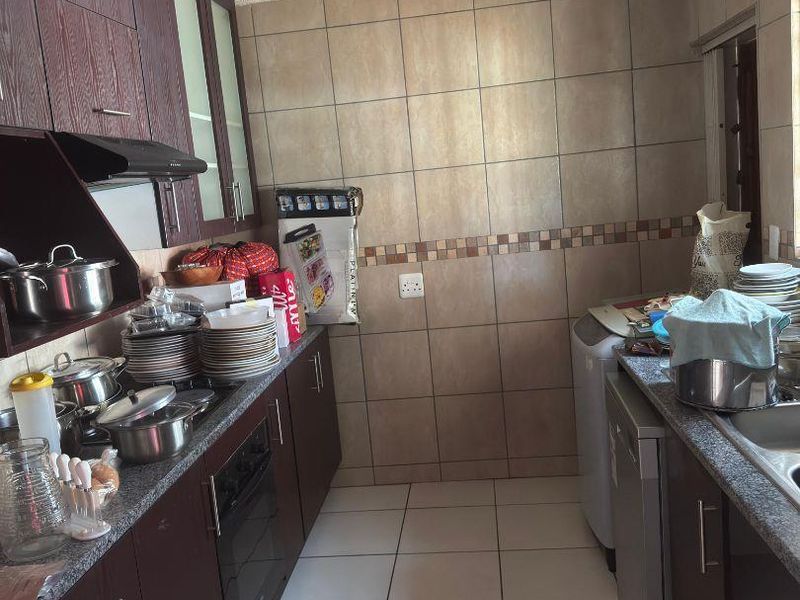 A functional kitchen featuring dark wood cabinetry, granite countertops, built-in oven, extractor fan, and tiled finishes throughout.