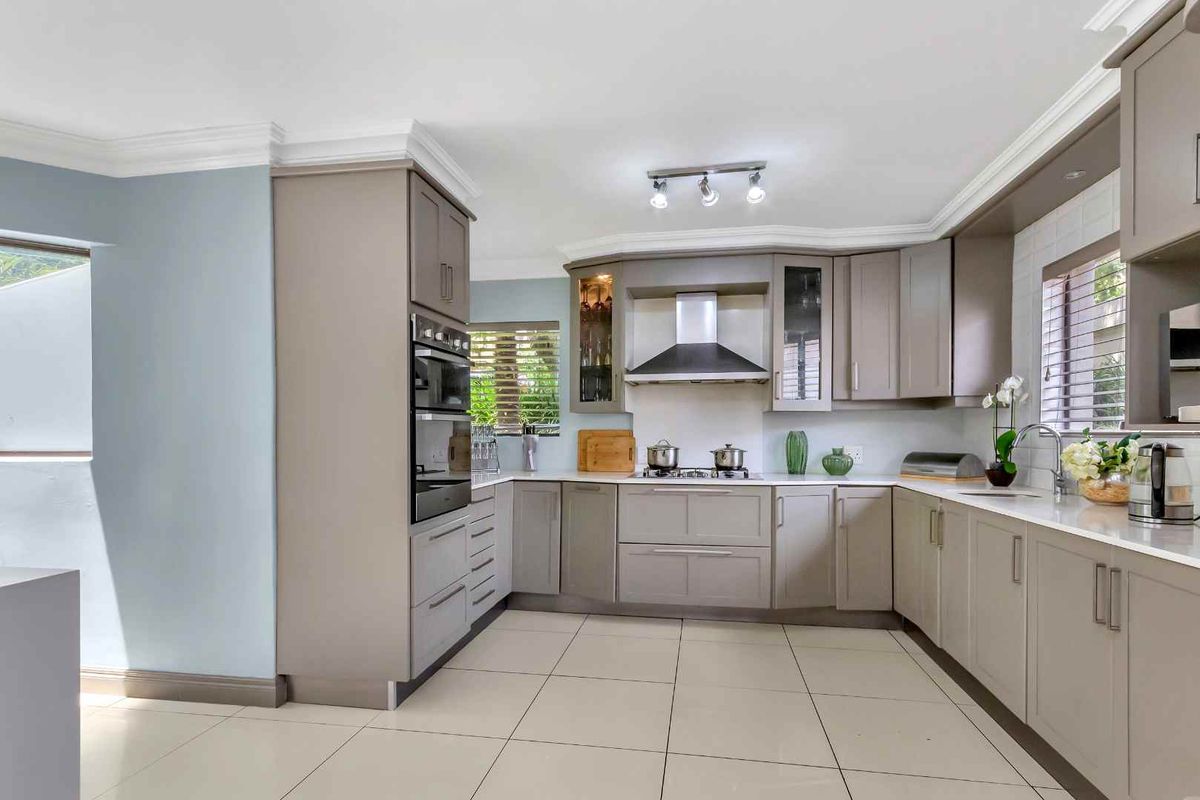 A modern kitchen featuring light grey cabinetry, stone countertops, a built-in oven, gas hob, and stainless steel extractor fan with tiled flooring.