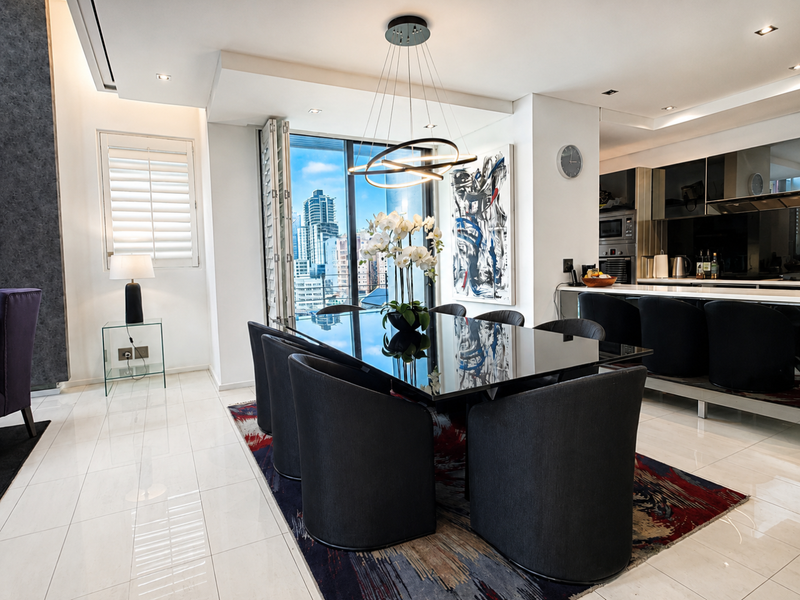 Modern open-plan living and dining area featuring sleek kitchen cabinetry, integrated appliances, high-gloss tiled floors, and large bi-fold doors opening to city views.